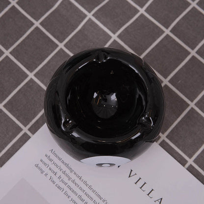 Bittchaser Supply Co. black ceramic 8-ball billiard ashtray with a glossy finish on a checkered tabletop surface.